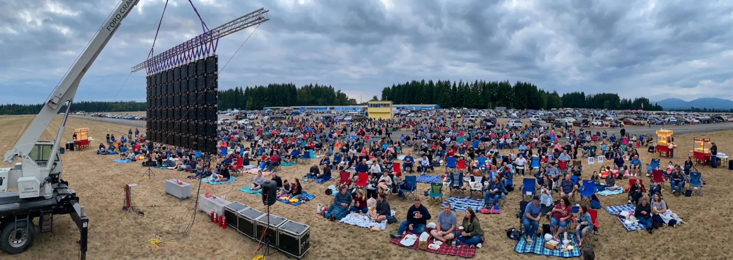 A packed movie night in Arlington: families on blankets and lawn chairs facing a City Park Events video wall hung from a crane