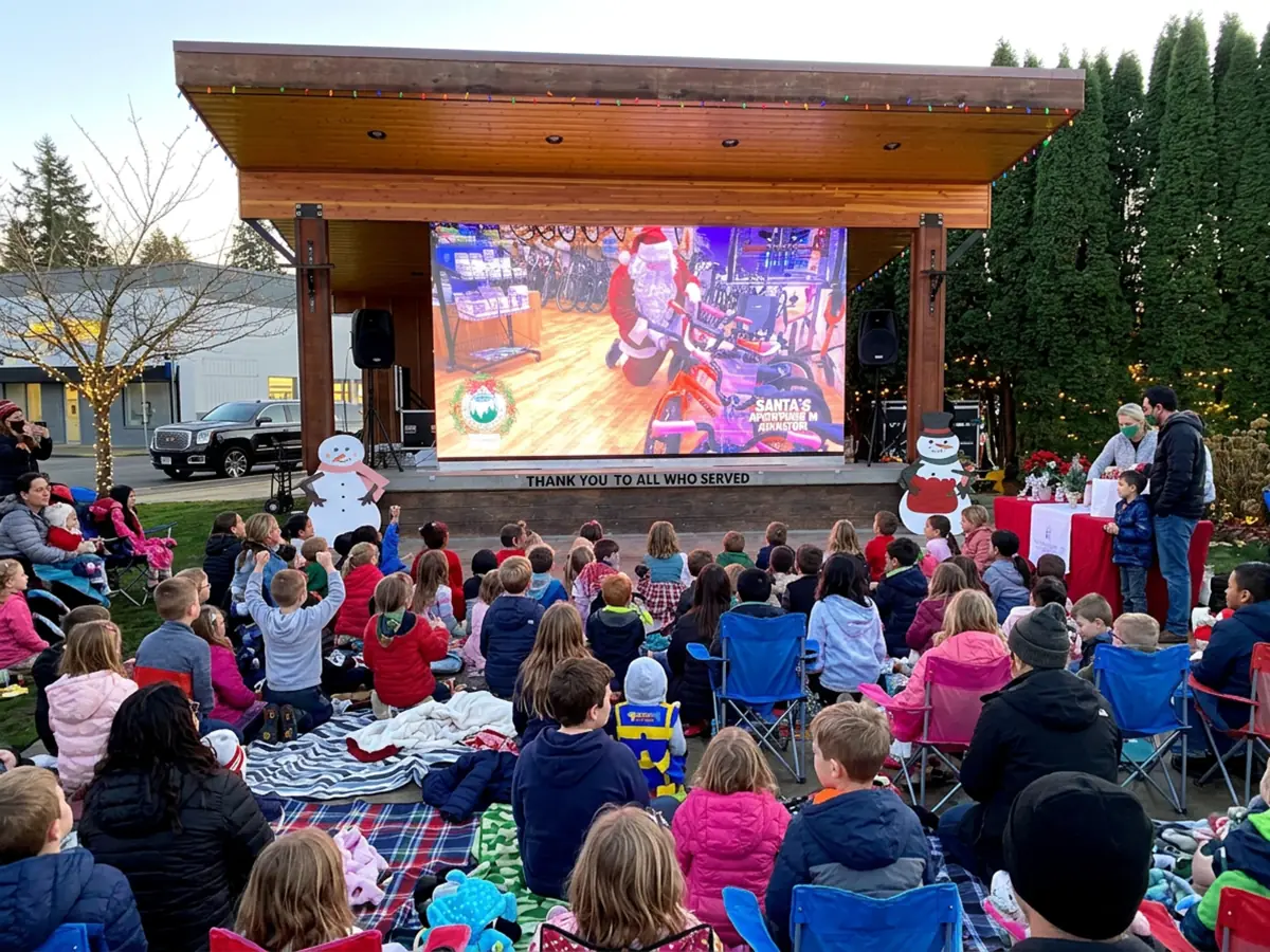 Kids on blankets watching a holiday movie on a City Park Events video wall under an outdoor stage